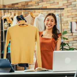 mulher segurando blusa caqui em um cabide para anunciar no seu ecommerce, uma nova forma do que vender para ganhar dinheiro